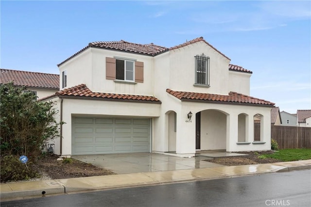 mediterranean / spanish-style home with a tile roof, stucco siding, concrete driveway, fence, and a garage