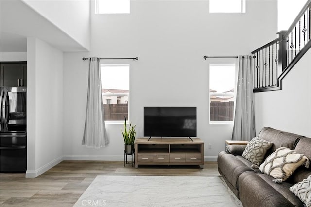 living area with baseboards, a high ceiling, stairs, and light wood-style floors