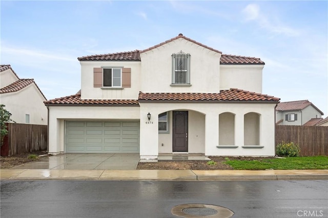 mediterranean / spanish-style home with a tile roof, stucco siding, fence, a garage, and driveway