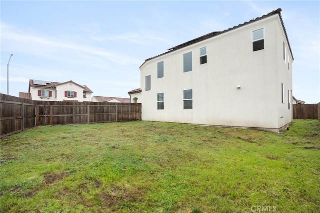 rear view of house featuring a fenced backyard, a lawn, and stucco siding