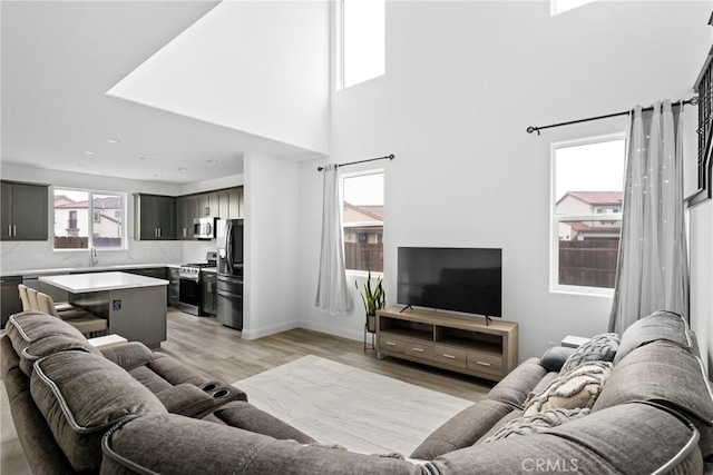 living area with light wood-style flooring, a high ceiling, and baseboards