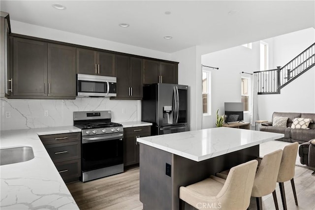 kitchen featuring stainless steel appliances, open floor plan, light wood finished floors, and light stone countertops