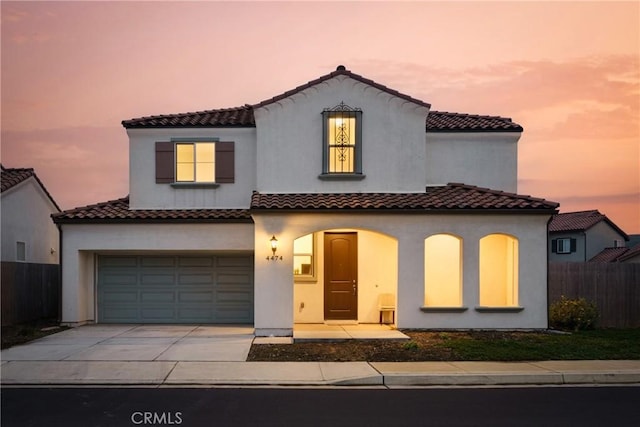 mediterranean / spanish house with fence, driveway, an attached garage, and stucco siding