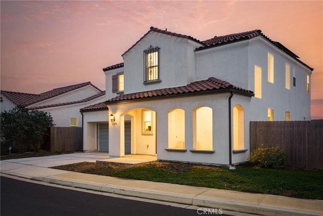 mediterranean / spanish house with driveway, stucco siding, fence, and a tiled roof