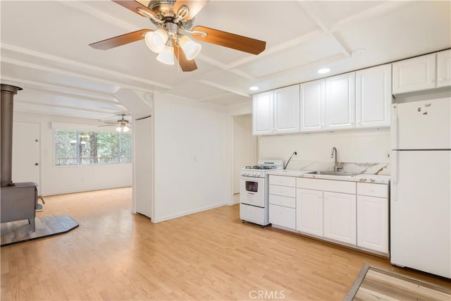 kitchen with light wood-style flooring, a wood stove, white cabinetry, a sink, and white appliances