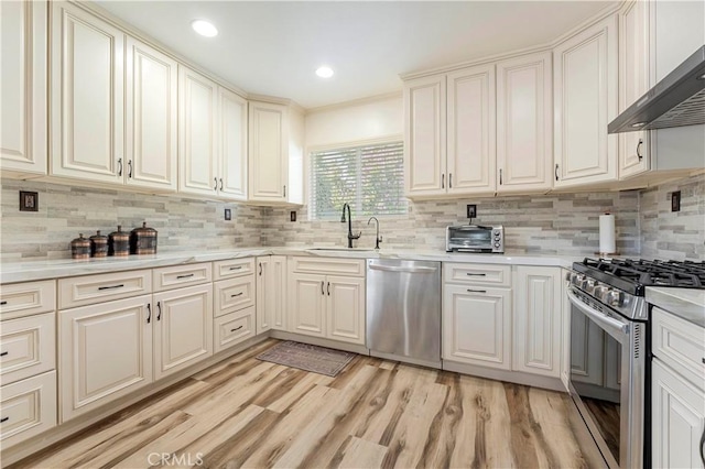 kitchen with stainless steel appliances, wall chimney exhaust hood, a sink, and light countertops