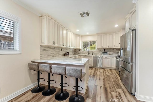 kitchen featuring tasteful backsplash, visible vents, a peninsula, stainless steel appliances, and a sink