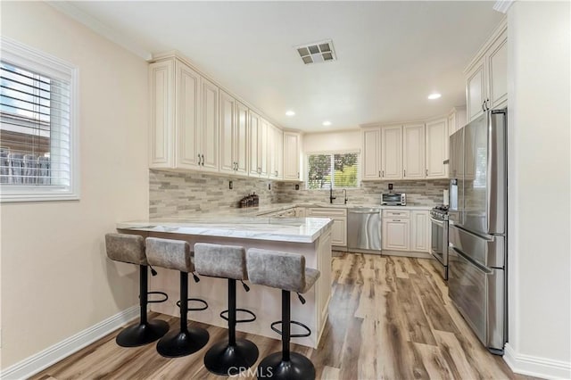 kitchen with a sink, a peninsula, decorative backsplash, light wood-style floors, and appliances with stainless steel finishes