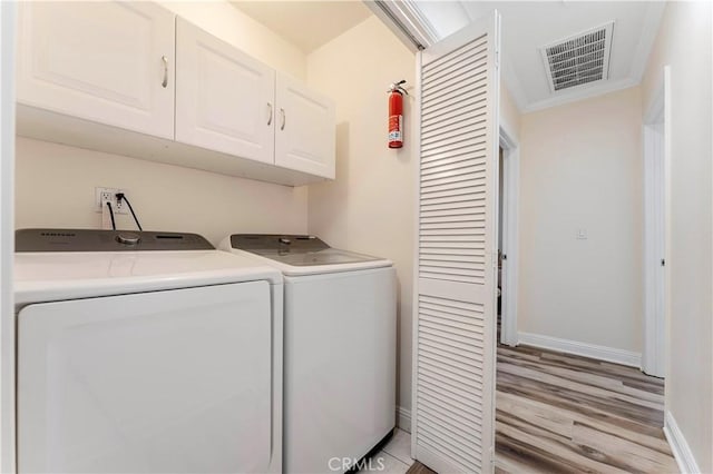 washroom with visible vents, light wood-style floors, baseboards, cabinet space, and washing machine and clothes dryer