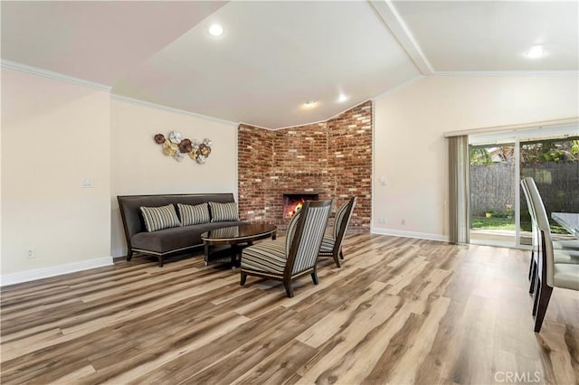 living room featuring lofted ceiling, a brick fireplace, crown molding, and wood finished floors