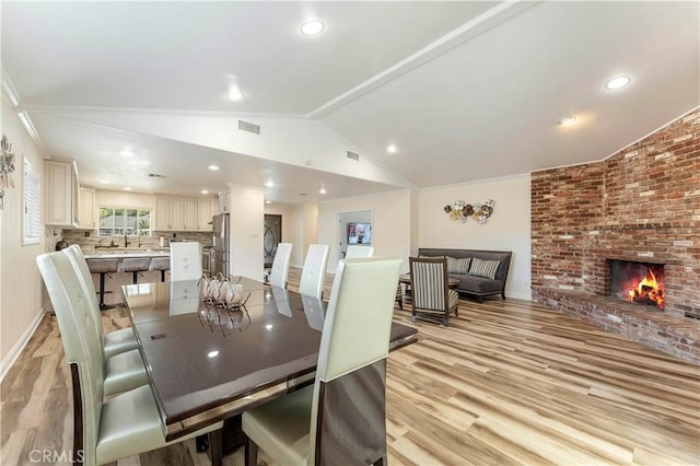 dining space with visible vents, a brick fireplace, vaulted ceiling, light wood-type flooring, and baseboards