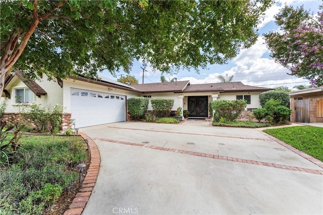 single story home with an attached garage, solar panels, brick siding, concrete driveway, and stucco siding