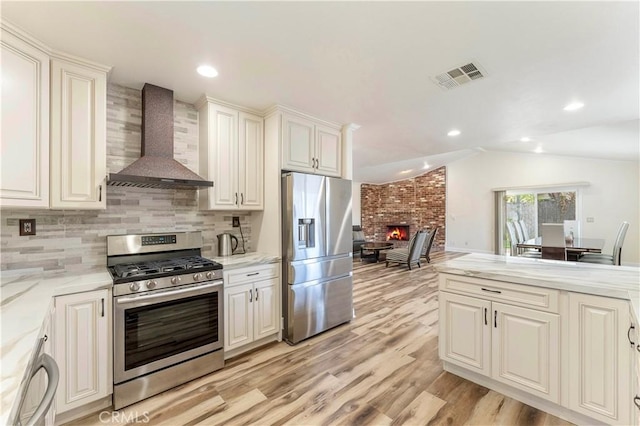 kitchen with visible vents, wall chimney exhaust hood, appliances with stainless steel finishes, vaulted ceiling, and a fireplace