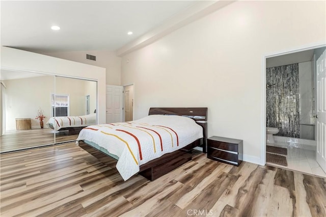bedroom with vaulted ceiling, a closet, visible vents, connected bathroom, and wood finished floors