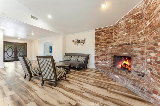 living area featuring a brick fireplace, wood finished floors, visible vents, and crown molding