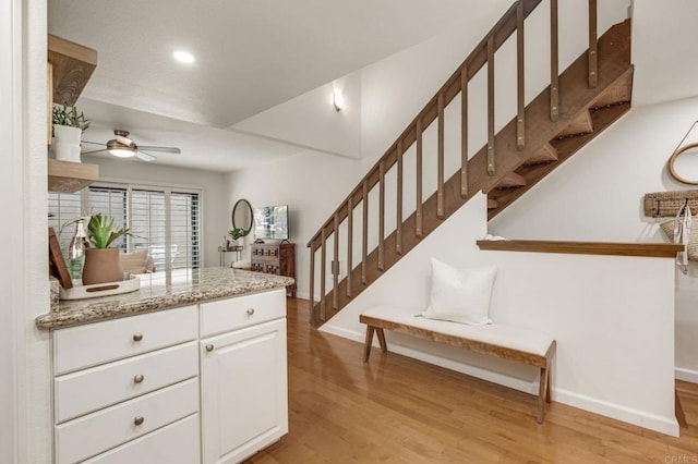 kitchen with baseboards, light wood finished floors, light stone countertops, and white cabinets