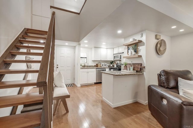 kitchen with light wood-style flooring, stainless steel appliances, a peninsula, white cabinetry, and light stone countertops