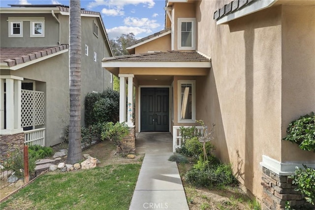 view of exterior entry with stucco siding and a tiled roof