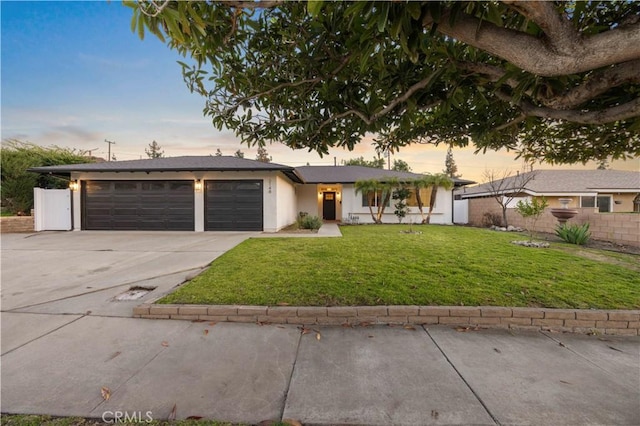 view of front of home featuring an attached garage, fence, driveway, a lawn, and stucco siding