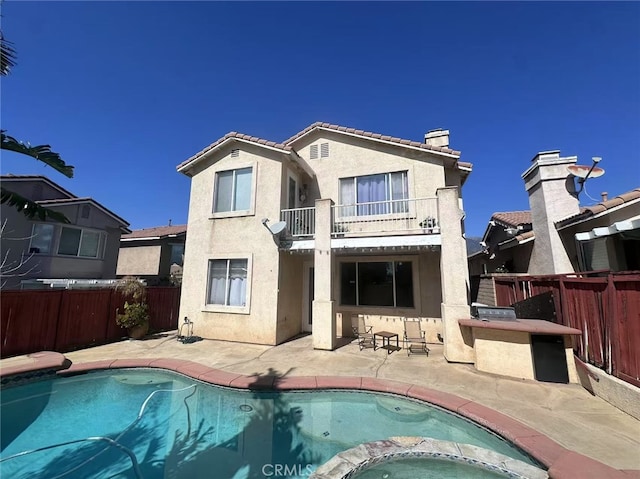 back of house with a balcony, fence, a tiled roof, stucco siding, and a patio area