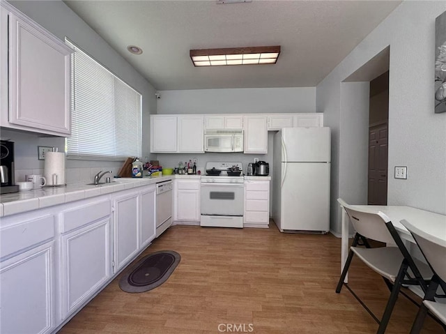 kitchen featuring white appliances, tile counters, white cabinets, light wood-style floors, and a sink