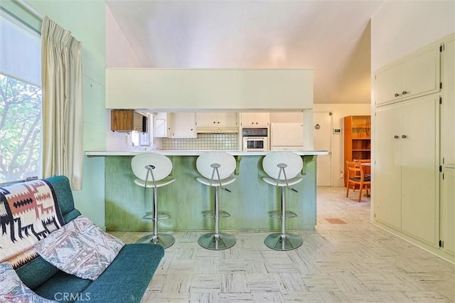 kitchen with white appliances, a breakfast bar, a peninsula, light countertops, and cream cabinetry