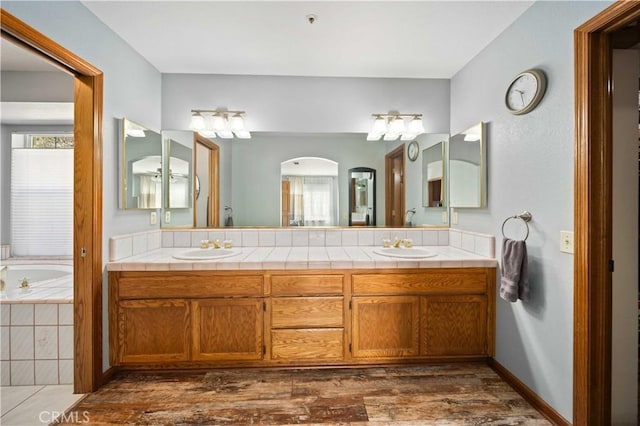 bathroom with a garden tub, double vanity, a sink, wood finished floors, and baseboards