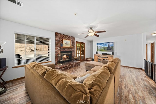 living room with a brick fireplace, wood finished floors, visible vents, and baseboards