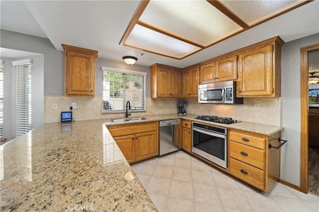 kitchen with light tile patterned floors, decorative backsplash, light stone counters, stainless steel appliances, and a sink