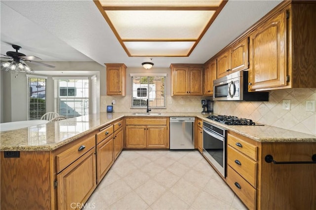 kitchen with brown cabinets, appliances with stainless steel finishes, a sink, light stone countertops, and a peninsula