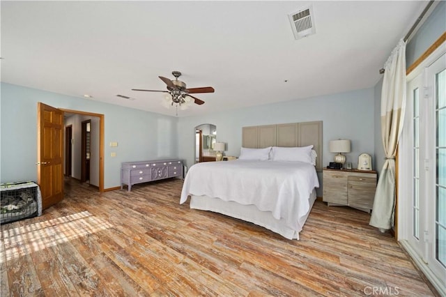 bedroom featuring light wood-style floors, visible vents, arched walkways, and a ceiling fan