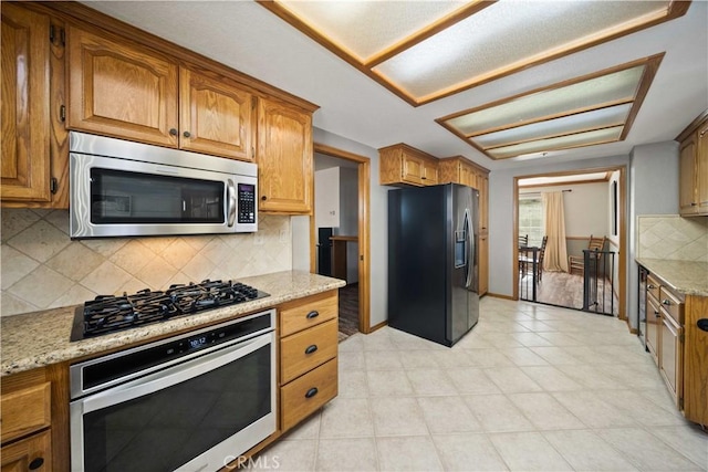 kitchen with black appliances, tasteful backsplash, brown cabinetry, and light stone countertops