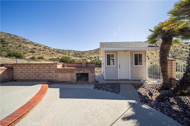 doorway to property featuring a patio area, a mountain view, fence, and roof with shingles