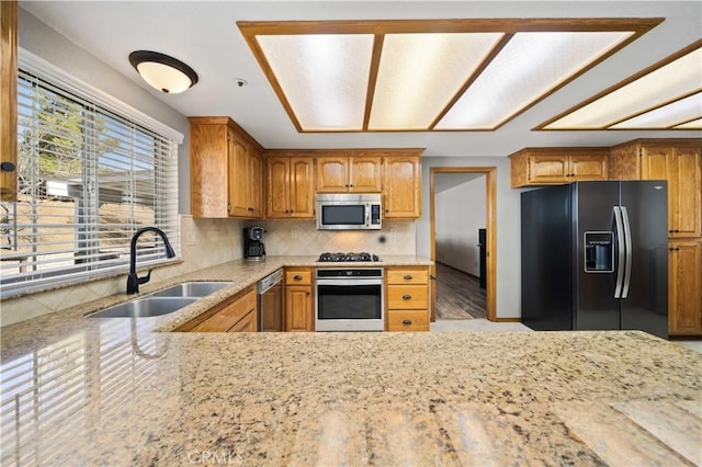 kitchen featuring a sink, appliances with stainless steel finishes, backsplash, light stone countertops, and brown cabinetry