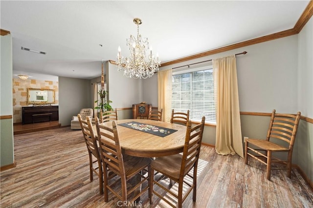 dining room featuring a chandelier, wood finished floors, visible vents, baseboards, and ornamental molding