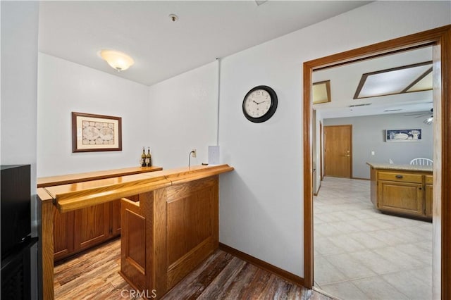 bar featuring light wood finished floors, indoor wet bar, and baseboards