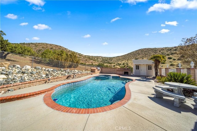 view of swimming pool featuring an outbuilding, a pool with connected hot tub, a patio area, a mountain view, and a fenced backyard