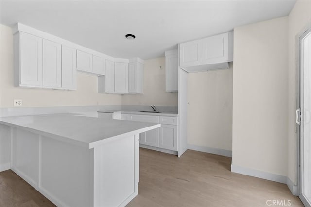 kitchen with light wood-type flooring, white cabinetry, a sink, and a peninsula