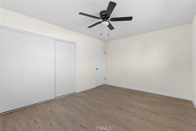 unfurnished bedroom with ceiling fan, a closet, baseboards, and wood finished floors