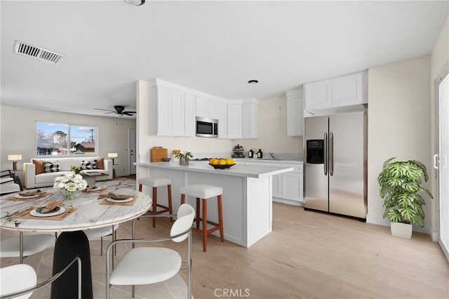 kitchen with visible vents, stainless steel appliances, light countertops, a kitchen bar, and white cabinetry