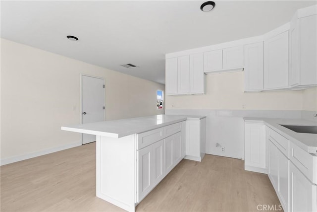 kitchen with a sink, visible vents, white cabinets, light countertops, and light wood-type flooring