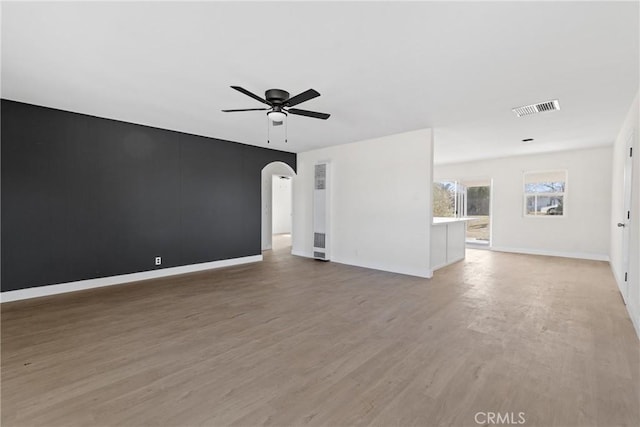 empty room with arched walkways, visible vents, light wood-style flooring, a ceiling fan, and baseboards