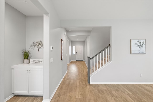 hallway featuring light wood finished floors, stairs, and baseboards