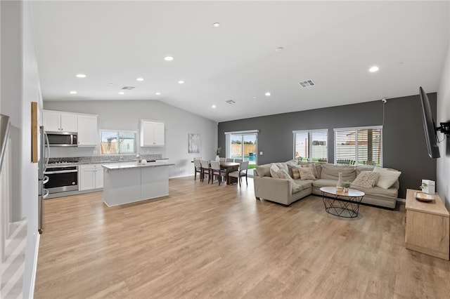 living area with light wood finished floors, visible vents, a wealth of natural light, and vaulted ceiling