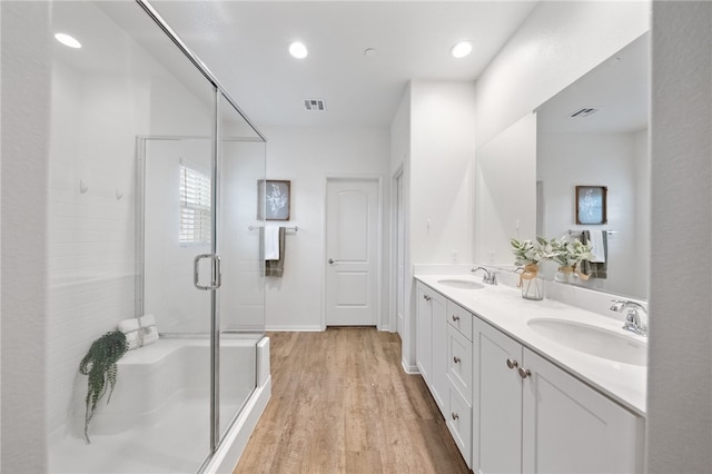 full bathroom featuring visible vents, a sink, wood finished floors, a shower stall, and double vanity