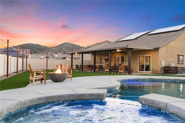 pool at dusk with a jacuzzi, a fenced backyard, a fire pit, ceiling fan, and a patio area