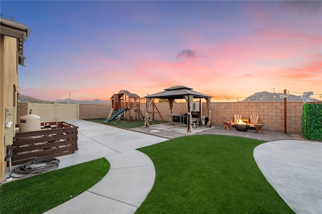 yard at dusk featuring a playground, an outdoor fire pit, a gazebo, a fenced backyard, and a patio area