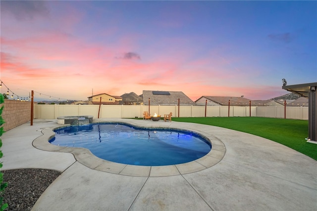 pool at dusk featuring a yard, a pool with connected hot tub, a fenced backyard, and a patio area