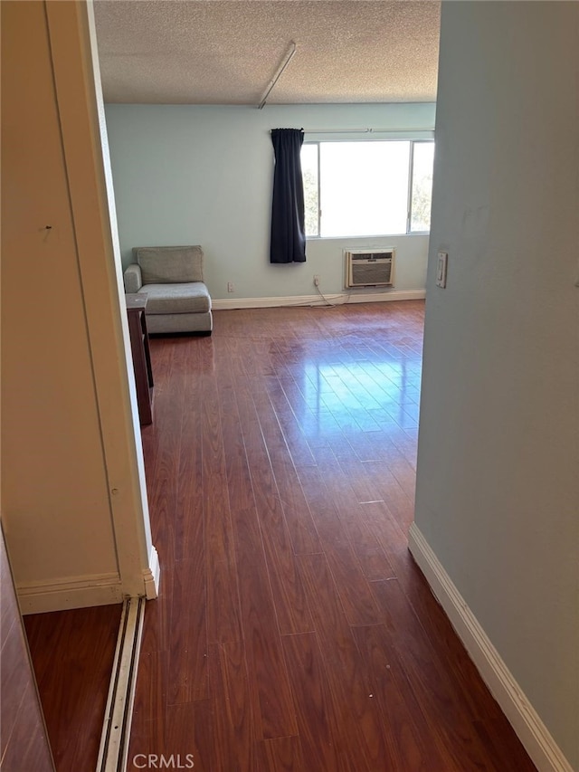 interior space with a textured ceiling, baseboards, dark wood-style flooring, and an AC wall unit