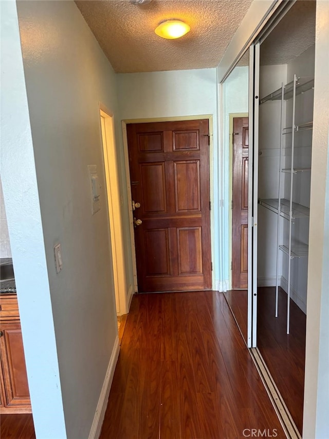 hallway featuring dark wood finished floors, a textured ceiling, and baseboards